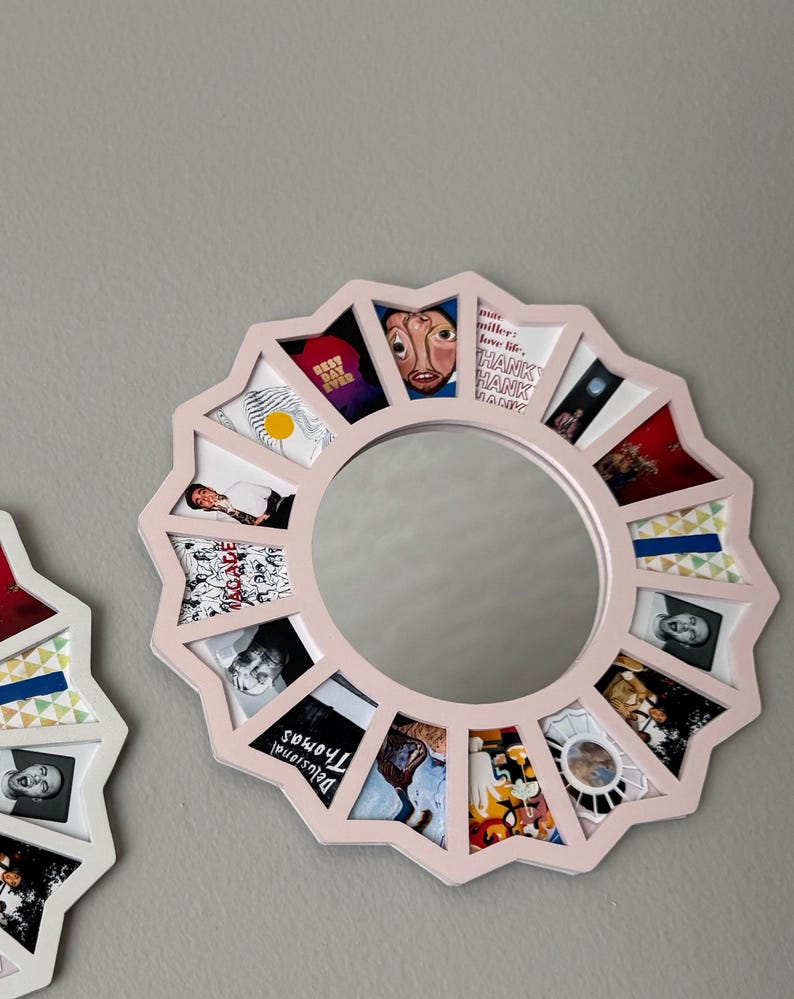 May include: A circular wall mirror with a light pink, star-shaped frame featuring twelve trapezoidal compartments surrounding the central glass. Each compartment displays a unique small image, including text such as "Best Day Ever" and "Delusional Thomas."