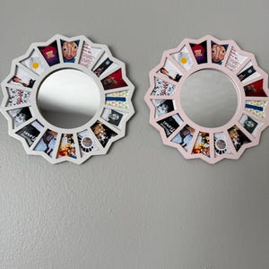 May include: Two circular wall mirrors with scalloped edges, one white and one light pink. Each frame features twelve trapezoidal compartments surrounding the central glass, containing various small graphic prints and album art imagery.