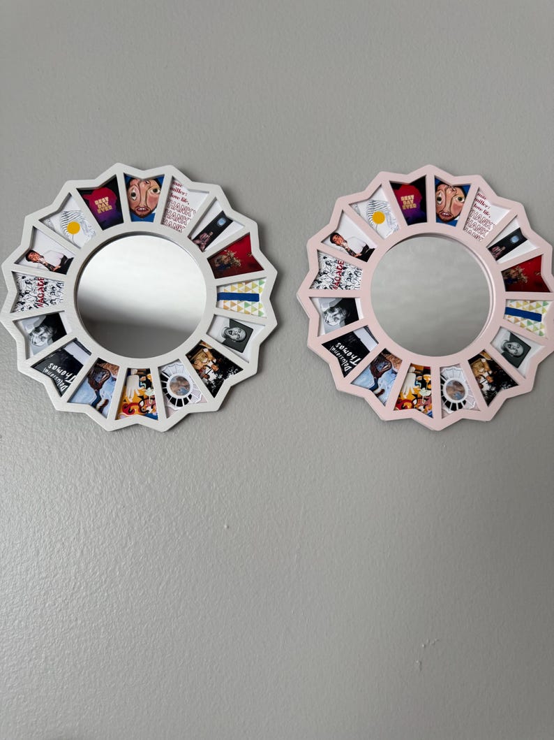 May include: Two circular wall mirrors with scalloped edges, one white and one light pink. Each frame features twelve trapezoidal compartments surrounding the central glass, containing various small graphic prints and album art imagery.