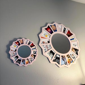 May include: Two circular mirrors with light pink frames, each featuring a sunburst-style border composed of multiple small, trapezoidal photo slots surrounding the central glass. The frames hold various colourful printed images in each slot.