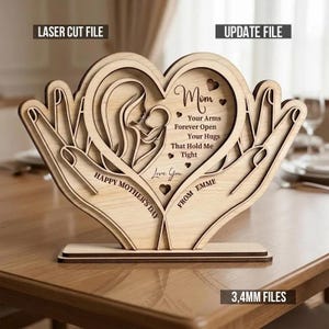 Op de afbeelding: Houten Moederdagdecoratie met een hartvormig ontwerp met een silhouet van moeder en kind, vastgehouden in handen. De tekst bevat "Mom", "Happy Mother's Day" en een persoonlijke boodschap. Gemaakt van gelaagd hout.
