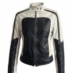 May include: A two-tone jacket featuring a central black panel on the front and back, contrasted by white side panels and sleeves. The jacket includes a high collar with two silver-toned snap buttons, a full-length front zipper, and visible stitching.