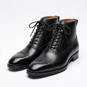May include: A pair of black leather lace-up boots featuring a cap toe design with decorative brogue perforations along the seams. These ankle-high boots include black laces, a stacked heel, and a smooth finish, presenting a structured silhouette.