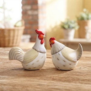 May include: A pair of ceramic chicken figurines featuring a rooster and a hen. Both birds have white bodies with light tan wing details, red combs, and red wattles. The rooster stands upright with a prominent tail, while the hen is positioned lower.