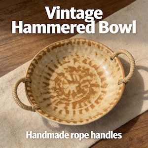 May include: Vintage hammered bowl with handmade rope handles. The bowl has a light brown and beige color scheme with a textured surface and a circular pattern. The handles are made of twisted rope.