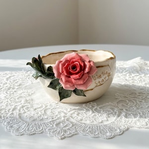 May include: A white ceramic mug with a black handle and the text "But First, Coffee" in a black, handwritten-style font. The mug is on a white surface.