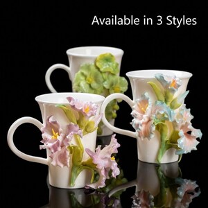 May include: Three white ceramic mugs with floral designs. One mug features green flowers, another has pink and purple flowers, and the third has pink and blue flowers. The text "Available in 3 Styles" is at the top.