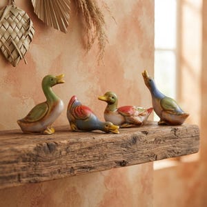 Puede incluir: Un conjunto de cuatro figuras de patos de cerámica expuestas en un estante de madera rústica. Los patos presentan posturas y paletas de colores variadas, incluyendo tonos verdes, azules, rojos y marrones, con acabados brillantes y detalles.