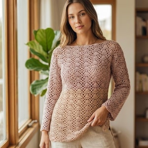 May include: A long-sleeved, open-weave crochet top in a gradient of pink to beige. The top has a boat neck and a slightly flared sleeve. The crochet pattern creates an open, airy design. The garment is a light, neutral color, suitable for layering.