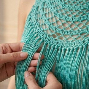 Pode incluir: Close-up de um top de croch&ecirc; turquesa com detalhe de franjas. O top apresenta um design circular vazado com franjas na borda inferior. A textura do croch&ecirc; &eacute; vis&iacute;vel, e a cor &eacute; um turquesa vibrante.