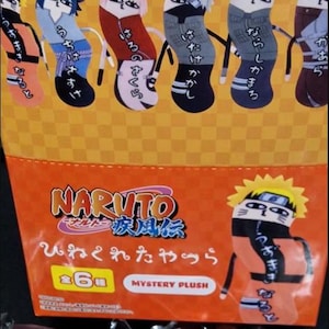 May include: Orange and yellow packaging featuring Naruto characters as plush toys. The packaging includes the Naruto logo and Japanese text. The plush toys are in the shape of socks and feature various characters from the anime series.