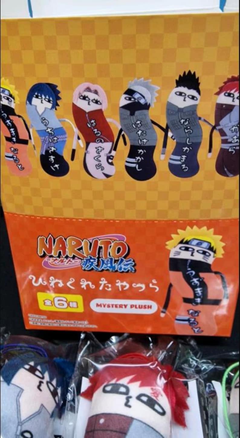 May include: Orange and yellow packaging featuring Naruto characters as plush toys. The packaging includes the Naruto logo and Japanese text. The plush toys are in the shape of socks and feature various characters from the anime series.