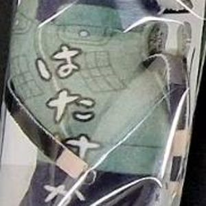 May include: A plush toy of a character from an anime series, packaged in clear plastic. The toy features a white-haired character with a headband and a green and blue outfit. The Japanese text "はたけ" is visible on the outfit.