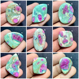 May include: A collection of nine polished cabochon gemstones featuring a mix of vibrant magenta-pink ruby inclusions embedded within a light green fuchsite matrix. Each stone displays unique natural patterns, varying shapes, and smooth surfaces.