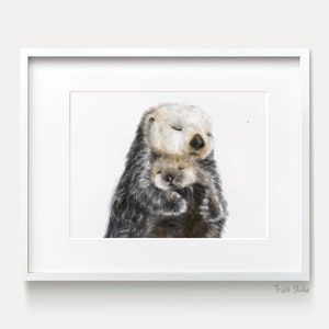 May include: A framed watercolor print featuring two sea otters. The larger otter, with a light beige face and dark fur, embraces a smaller otter. Both otters have their eyes closed, suggesting a peaceful moment. The print is set in a white frame.