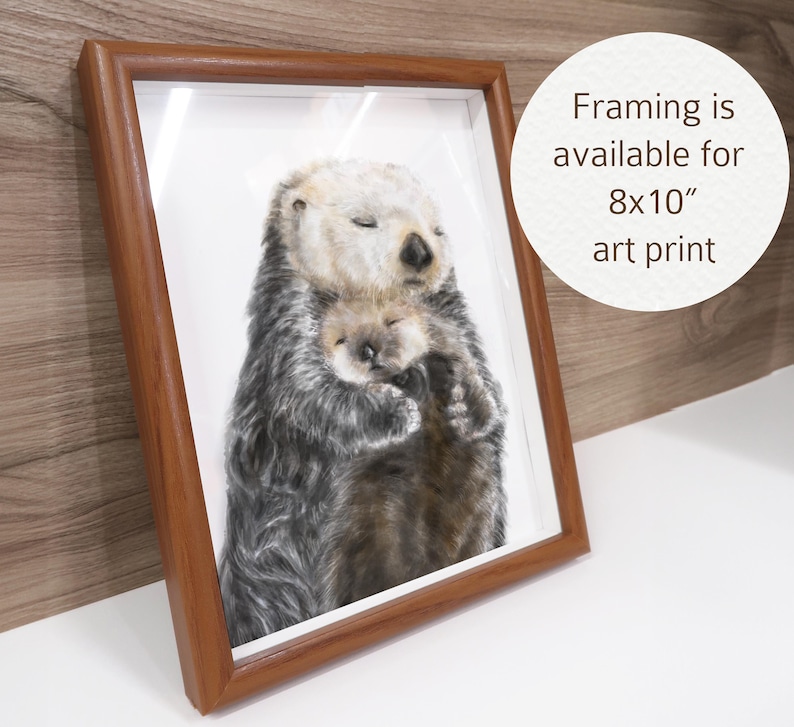 May include: A framed art print featuring a mother sea otter embracing her pup. The artwork is in a wooden frame and is available as an 8x10 inch print. The otters are depicted with realistic fur and closed eyes, creating a tender scene.
