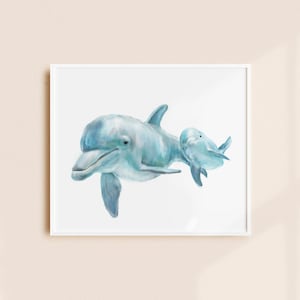Pu&ograve; includere: Dipinto ad acquerello di due delfini nelle tonalit&agrave; del blu e del verde acqua. Il delfino pi&ugrave; grande nuota accanto a uno pi&ugrave; piccolo, entrambi su sfondo bianco. L'opera &egrave; incorniciata in una cornice quadrata bianca, adatta a un tema costiero o nautico.