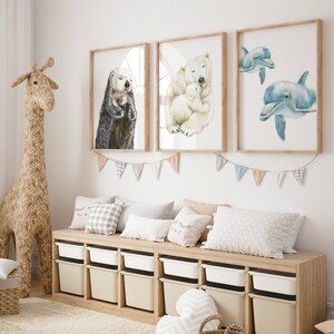 May include: A children's room with three framed watercolor prints of animals: an otter, a polar bear with a cub, and two dolphins. The room also features a woven giraffe, a wooden storage bench with white bins, and decorative pillows.