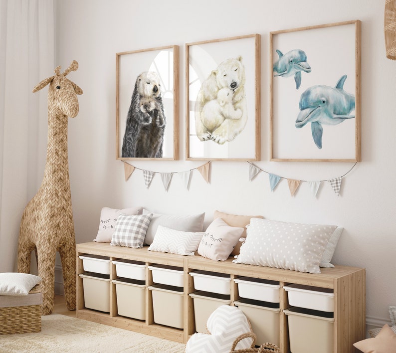 May include: A children's room with three framed watercolor prints of animals: an otter, a polar bear with a cub, and two dolphins. The room also features a woven giraffe, a wooden storage bench with white bins, and decorative pillows.