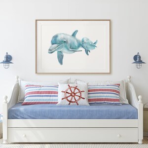 Pu&ograve; includere: Una stampa ad acquerello incorniciata di due delfini in tonalit&agrave; di blu. L'opera d'arte &egrave; appesa sopra un divano letto bianco con lenzuola blu e cuscini a righe. L'arredamento a tema nautico include un cuscino con un design a timone e applique blu.