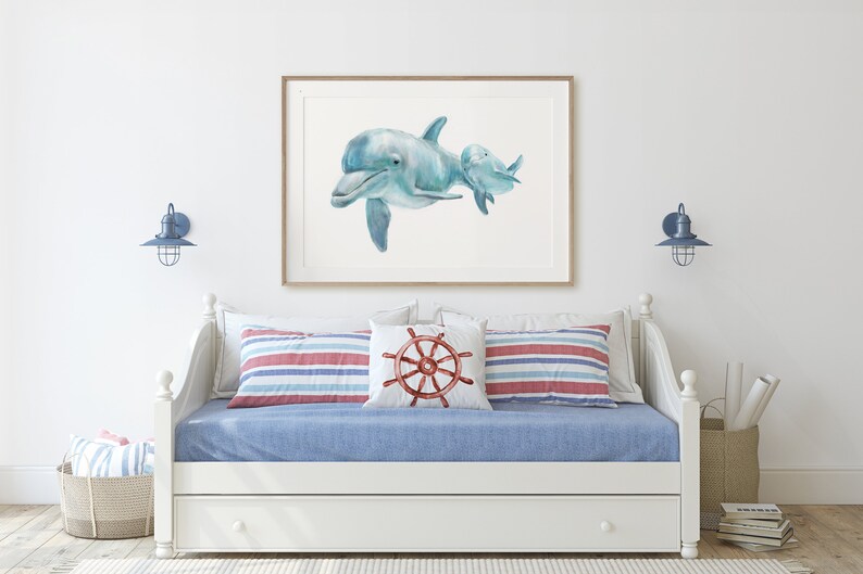 Pu&ograve; includere: Una stampa ad acquerello incorniciata di due delfini in tonalit&agrave; di blu. L'opera d'arte &egrave; appesa sopra un divano letto bianco con lenzuola blu e cuscini a righe. L'arredamento a tema nautico include un cuscino con un design a timone e applique blu.