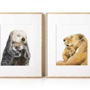 May include: Two framed art prints. One features a watercolor illustration of a sea otter cuddling its pup. The other depicts a lioness embracing her cub. Both artworks are in wooden frames, perfect for nursery or home decor.