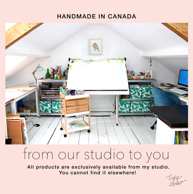 Pu&ograve; includere: Luminoso studio d'arte con tavolo da disegno, carrello e scaffali. Il testo "HANDMADE IN CANADA" e "from our studio to you" sono visibili. Lo studio &egrave; pieno di materiali artistici e un computer.