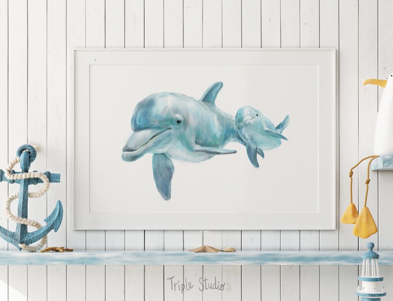 Pu&ograve; includere: Una stampa ad acquerello incorniciata con due delfini azzurri che nuotano insieme. L'opera d'arte &egrave; esposta su una mensola bianca con decorazioni nautiche, tra cui un'ancora blu e un gabbiano decorativo. Il testo "Triple Studio" &egrave; visibile.