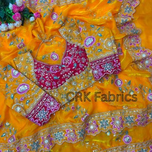 Puede incluir: Una tela de color amarillo brillante con una blusa rosa intenso que presenta intrincados bordados florales, lentejuelas y cuentas. La tela tiene un borde festoneado con motivos florales rosas y plateados. El texto CRK Fabrics es visible.