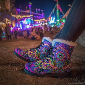 May include: A pair of colorful, patterned boots with a psychedelic design. The boots feature a mix of pink, purple, blue, and yellow hues, with a white faux fur trim around the top. The boots have black laces and soles.