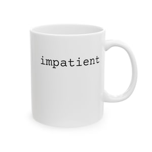 Op de afbeelding: Witte keramische mok met het woord "impatient" in zwarte letters. De mok heeft een gebogen handvat en een eenvoudig ontwerp, geschikt voor koffie, thee of andere dranken.