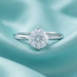 May include: A white ceramic mug with a black handle and the text "But First, Coffee" in a bold, black font. The mug is set against a blurred background, suggesting a cozy setting.