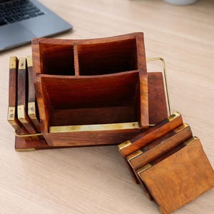 Op de afbeelding: Een houten bureau-organizer met meerdere compartimenten en een bijpassende set onderzetters. De organizer is gemaakt van donkerbruin hout met messing accenten. De onderzetters zijn vierkant en hebben ook messing hoeken.