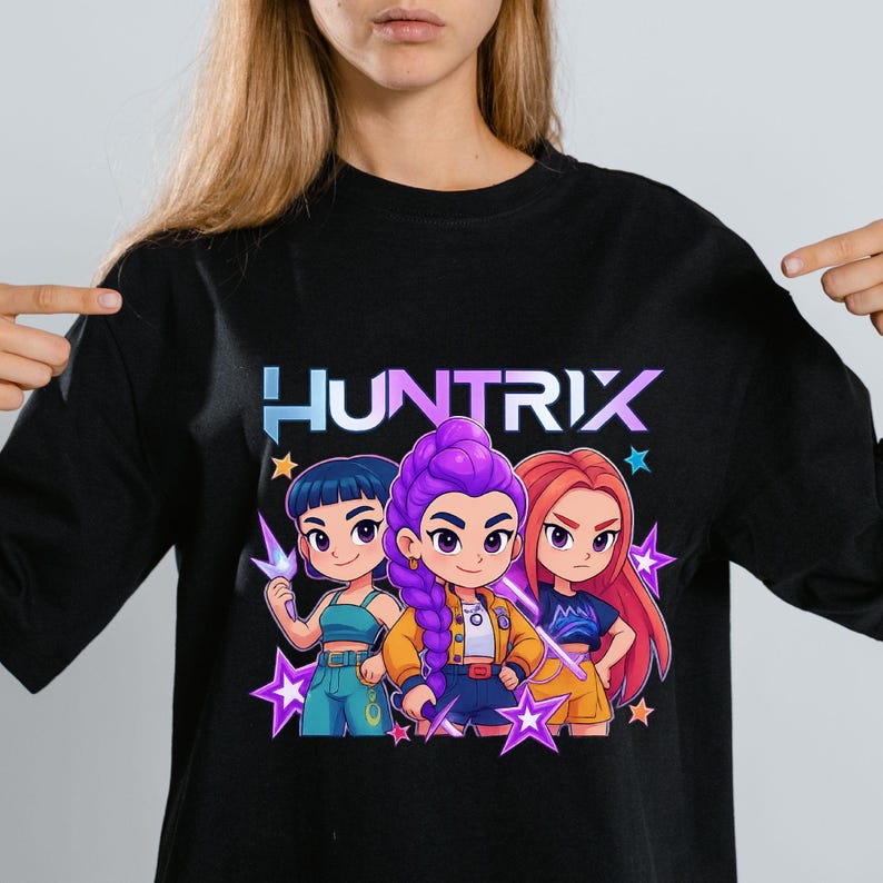 May include: Black long-sleeve shirt featuring the word "HUNTRIX" in a blue and purple gradient. The shirt has a graphic of three cartoon characters with different hair colors and outfits, surrounded by purple star shapes.