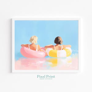 May include: A framed print featuring two people in swimsuits floating in inflatable rings. One ring is pink, the other is yellow and white. The background is a light blue sky and water with a soft, pastel color palette.