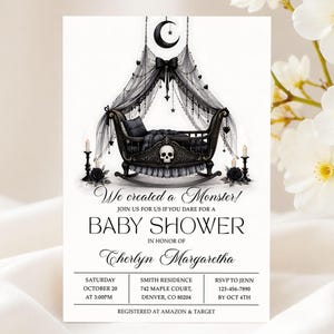 May include: A baby shower invitation card featuring a black rocking cradle with a skull motif, draped in sheer black fabric with a crescent moon and star mobile. Text reads: We created a Monster! JOIN US FOR US IF YOU DARE FOR A BABY SHOWER IN HONOR OF Cherlyn Margaretha.