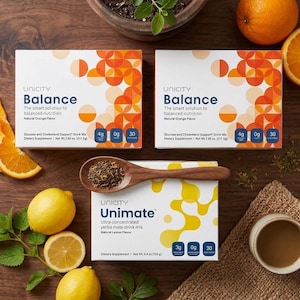 Puede incluir: Una vista cenital muestra cajas de Unicity Balance y Unimate, junto con limones, naranjas y una cuchara de madera con hojas de t&eacute;. Las cajas de Balance tienen dise&ntilde;os en naranja y blanco. La caja de Unimate es blanca con detalles amarillos.
