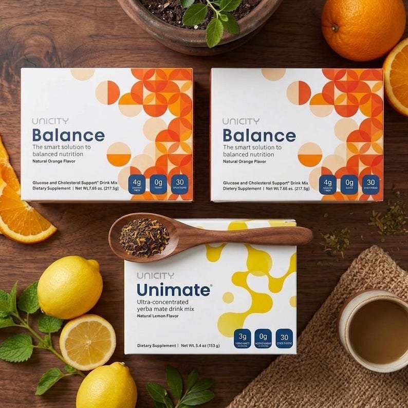 Puede incluir: Una vista cenital muestra cajas de Unicity Balance y Unimate, junto con limones, naranjas y una cuchara de madera con hojas de t&eacute;. Las cajas de Balance tienen dise&ntilde;os en naranja y blanco. La caja de Unimate es blanca con detalles amarillos.