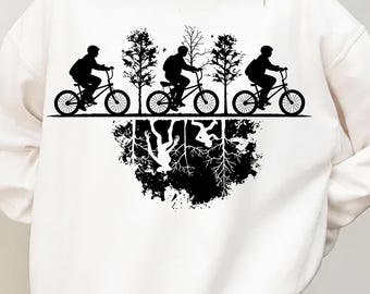 May include: White sweatshirt with a black graphic depicting three cyclists on bicycles, riding past trees. Beneath, a mirrored image shows an inverted world with roots and abstract shapes. The design is a silhouette.