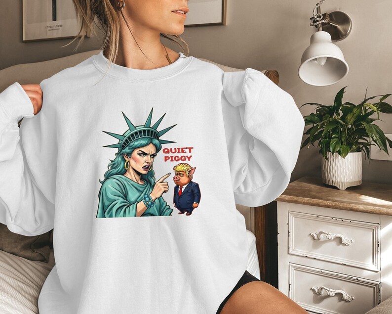 May include: White sweatshirt featuring a graphic of the Statue of Liberty pointing at a pig in a suit, with the text "QUIET PIGGY" in red. The Statue of Liberty is depicted with a stern expression.