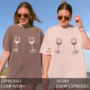 May include: Two short-sleeve crew neck t-shirts in espresso and ivory. Each shirt features two wine glass illustrations with text underneath. The espresso shirt reads The Bach and Emma's Bachelorette Napa Valley 2024. The ivory shirt reads The Bride and Emma's Bachelorette Napa Valley 2024.