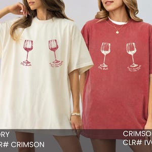 May include: An ivory t-shirt and a crimson t-shirt, each featuring two wine glass graphics. The ivory shirt has red text reading The Bride and Emma's Bachelorette Napa Valley 2024. The crimson shirt has white text reading The Bach and Emma's Bachelorette Napa Valley 2024.
