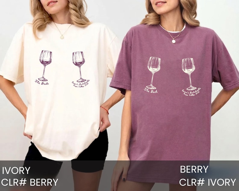 May include: Two short-sleeve crewneck t-shirts, one ivory and one berry, each featuring a graphic of two wine glasses. The ivory shirt has purple text reading The Bride and Emma's Bachelorette Napa Valley 2024. The berry shirt has white text.