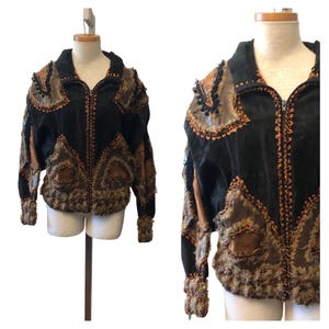 May include: A black and brown jacket featuring a front zipper closure, long sleeves, and a high collar. The garment is constructed with patchwork panels of black suede and brown leather, accented with decorative frayed edges and trim.