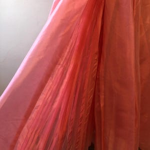 May include: A flowing, coral-colored garment with a pleated section. The fabric appears to be lightweight and has a slight sheen, suggesting a satin or silk-like material. The garment is likely a dress or skirt.