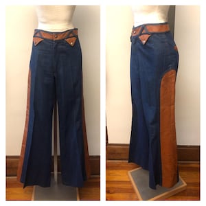 Op de afbeelding: Vintage blauwe spijkerbroek met bruine leren accenten. De broek heeft een hoge taille met een bruine leren tailleband en zijpanelen. De uitlopende pijpen geven een retro-stijl. De broek wordt op een mannequin gepresenteerd.