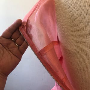 May include: Close-up of a pink dress with a zipper closure. The dress is made of a shiny, silky material. The zipper is silver and runs along the side of the dress. The dress is displayed on a mannequin.