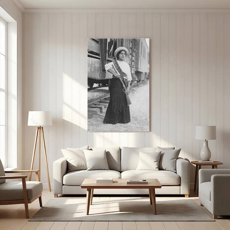 May include: Black and white print of a woman in a long skirt, white blouse, and hat, holding a rifle. She stands near a train, wearing a sash. The image is a vintage photograph, likely from the early 20th century, and is displayed as wall art.