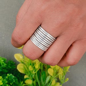 Puede incluir: Un conjunto de anillos apilables que consta de diez bandas individuales, finas, lisas y de color plateado que se usan juntas en un dedo. Las bandas tienen un perfil redondeado y un acabado metálico pulido, creando una apariencia uniforme.