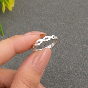 Op de afbeelding: Een zilverkleurige ring met een doorlopend, herhalend gedraaid of gevlochten patroon rondom de gehele band. Het metaal heeft een gladde, gepolijste afwerking die licht reflecteert, wat zorgt voor een heldere, metalen uitstraling over het oppervlak.
